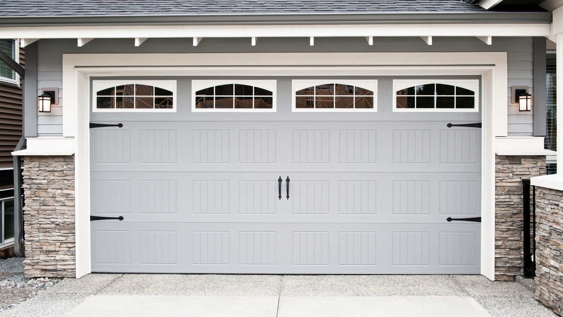 Modern white two-car garage door with arched windows and stone pillars on sides.