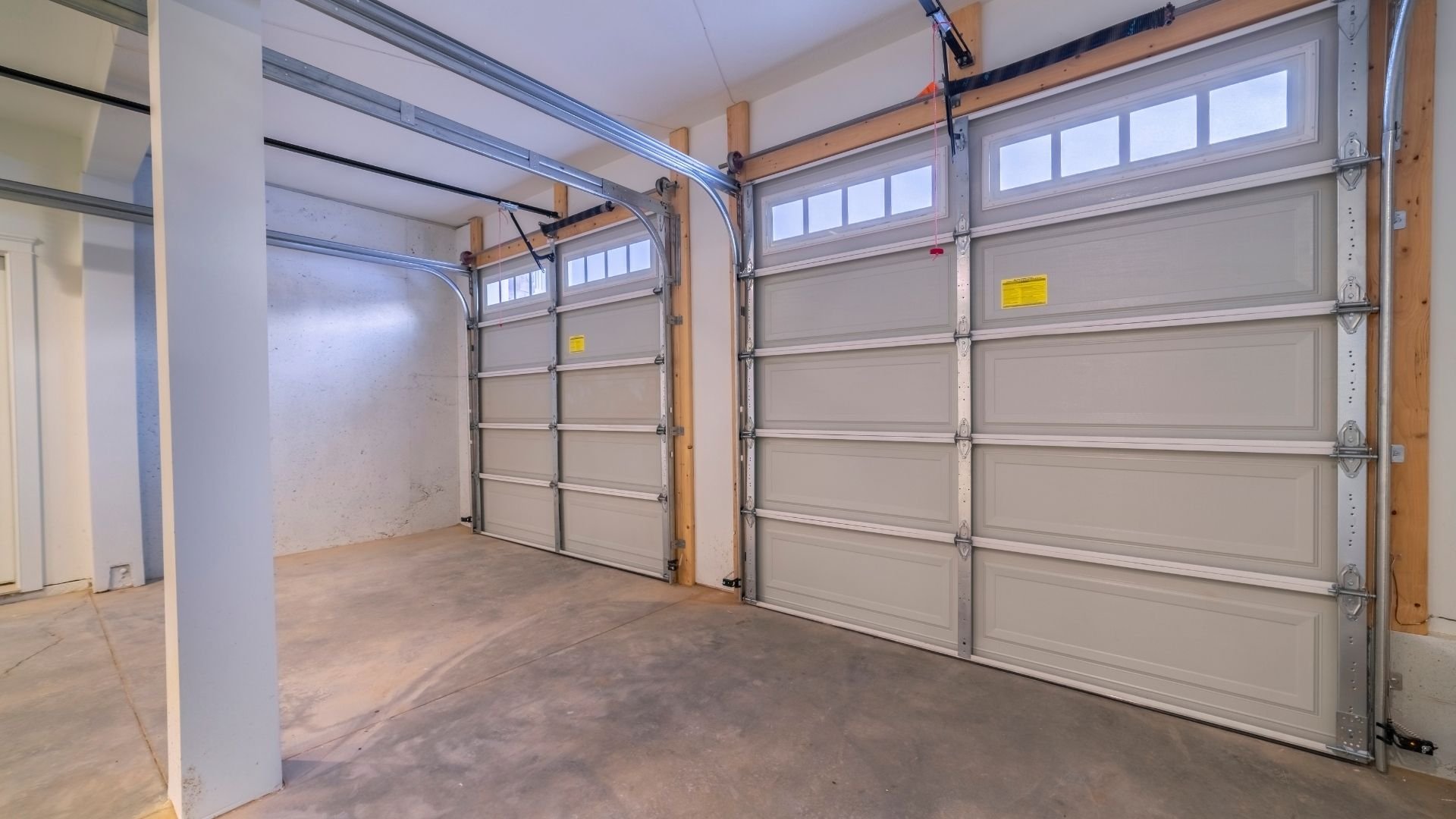 Empty garage interior with two gray sectional doors and concrete floor