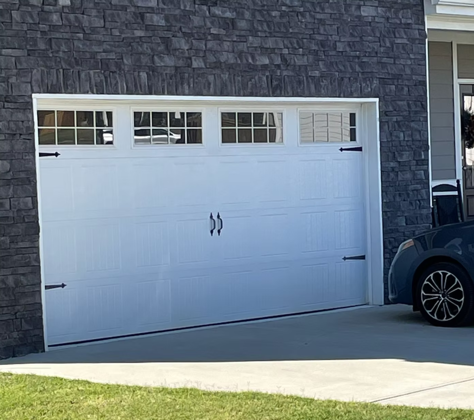 White garage door with windows on dark brick house, parked vehicle visible