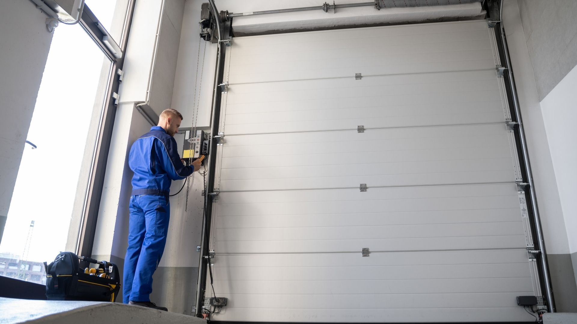 Technician in blue uniform inspects garage door mechanism with handheld device