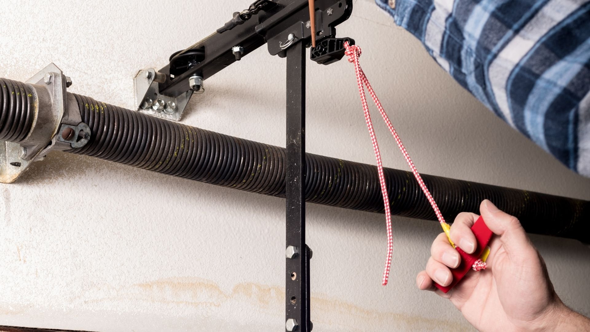 Technician adjusting garage door tension spring with red safety rope