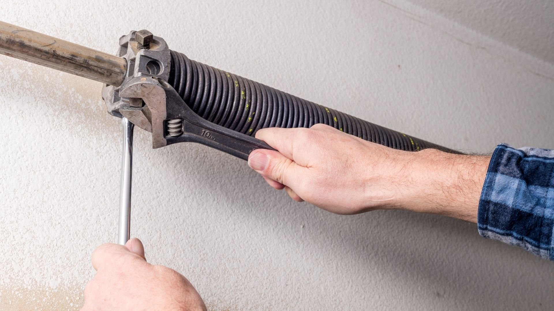 Person adjusting garage door spring with wrench against white wall