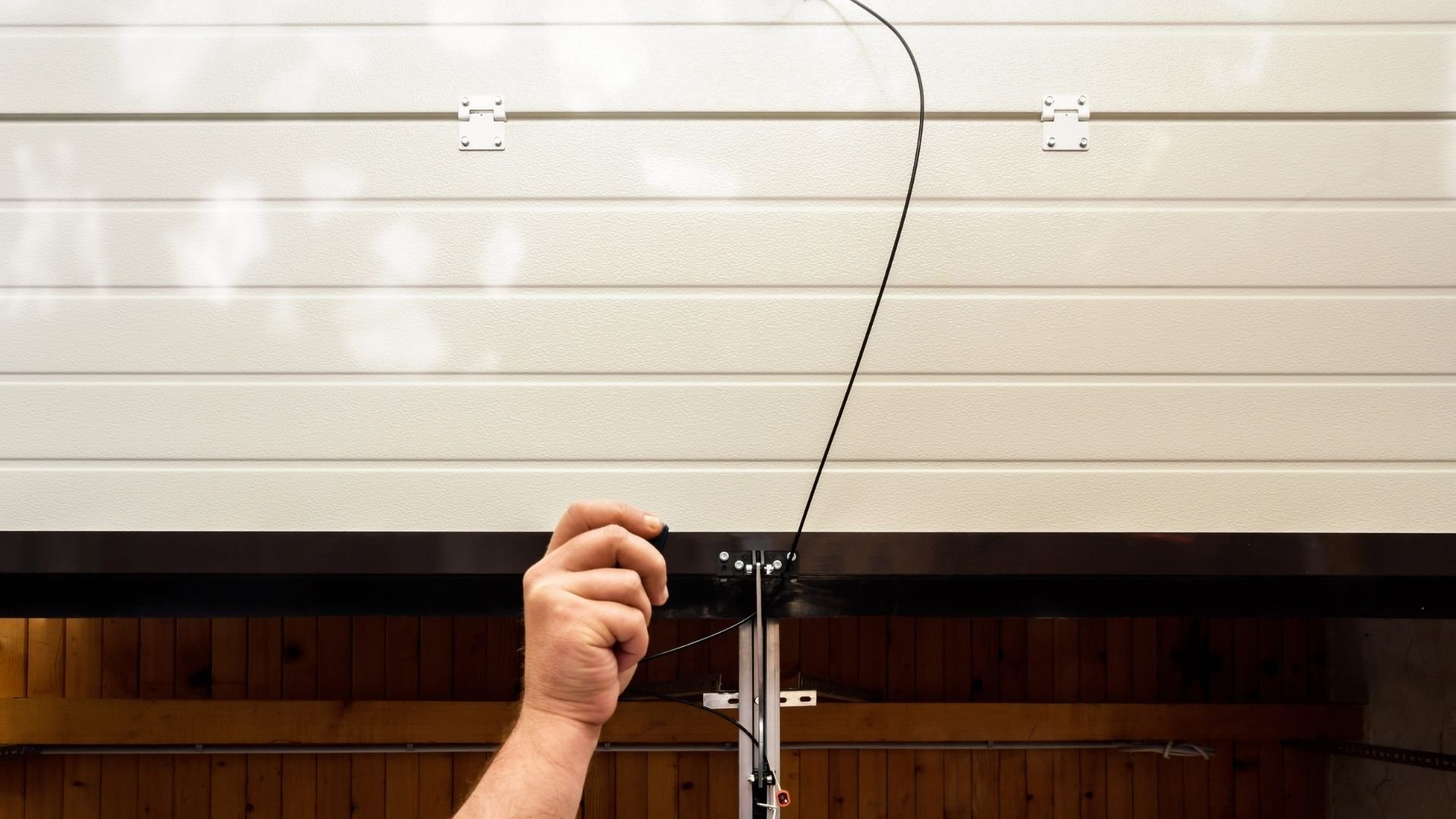 Hand pulling cable to open white garage door with wood siding below