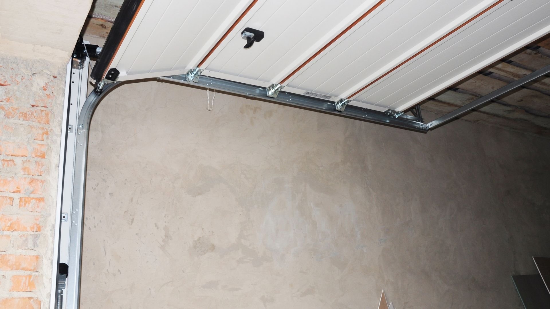 Overhead garage door mechanism showing white panels, metal frame, and opener mounted on ceiling