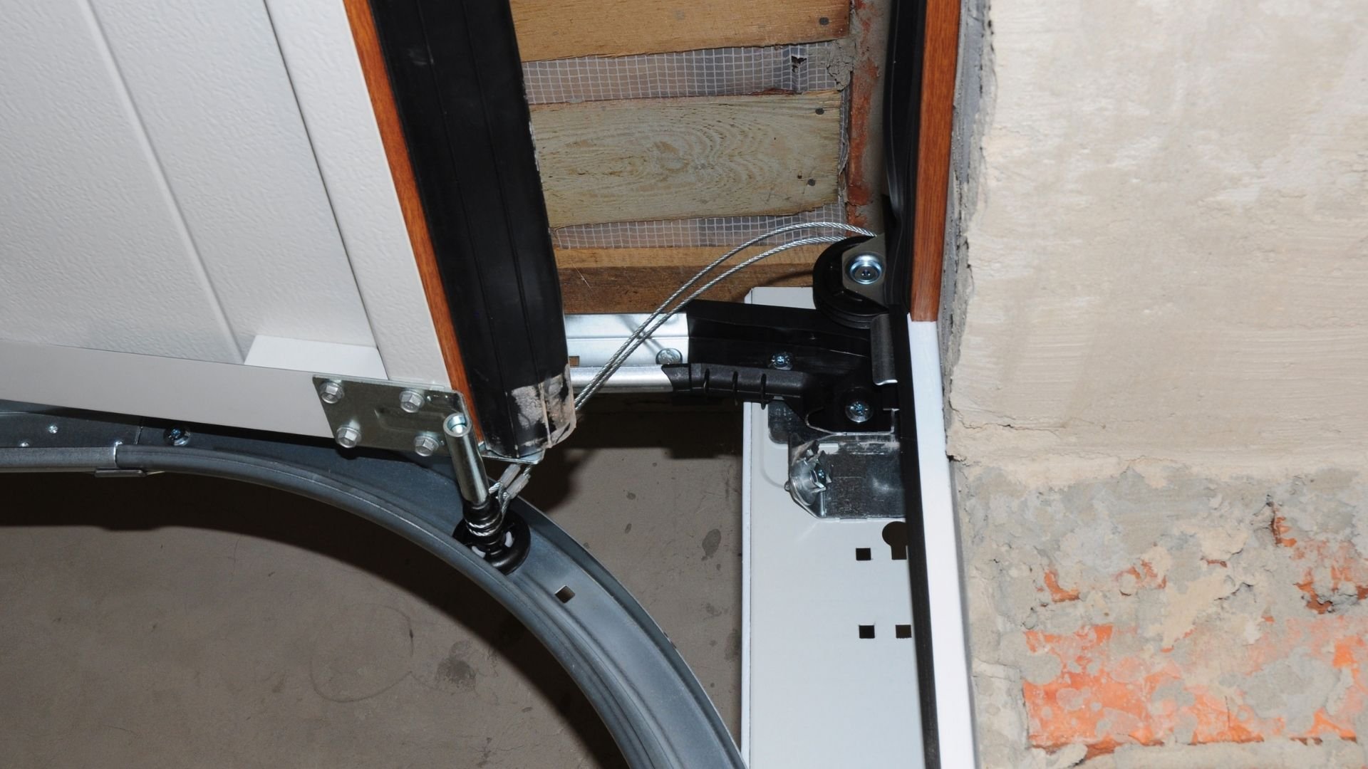 Garage door opener mechanism with metal brackets, cables, and electrical components mounted indoors